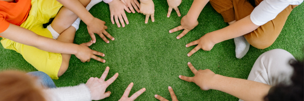 芝生の上で子どもたちが円になって手を合わせているイメージ写真