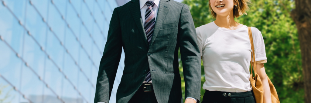 スーツ姿の男性と笑顔の女性が並んで歩くビジネスシーン。インターンとして活躍する若手社員のイメージ