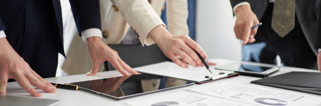 複数のビジネスパーソンがテーブルを囲み、資料やタブレットを使って議論しているイメージ写真
